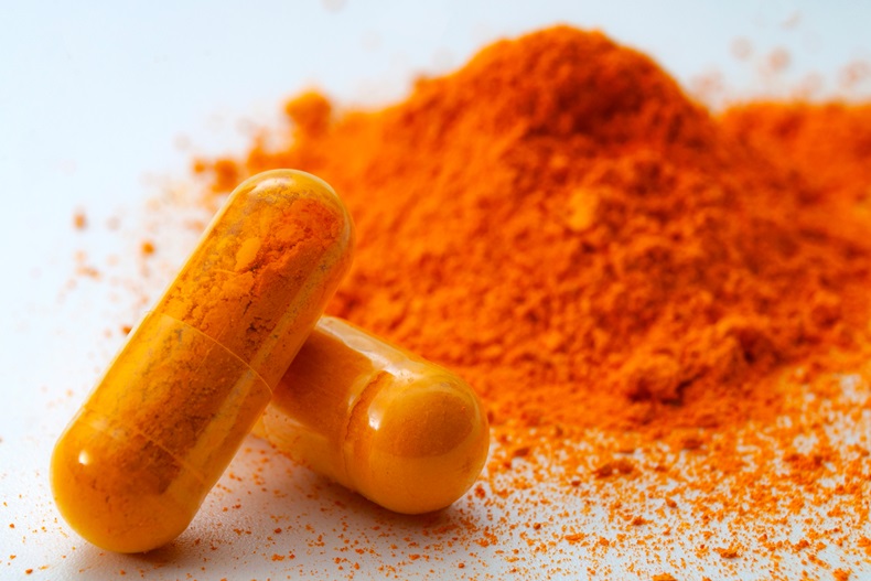 Alternative medicine, antioxidant food and herbal remedy concept theme with macro close up on supplement pill of curcumin or turmeric with a heap of the spice in dry powder form in the background - Image 