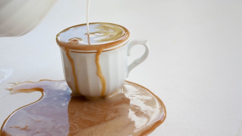 overflowing coffee cup with coffee spilled on table