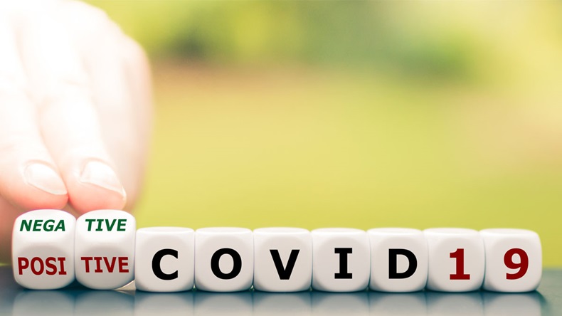 Test result of a Corona test. Hand turns a dice and changes the expression "positive COVID19" to "negative COVID19".