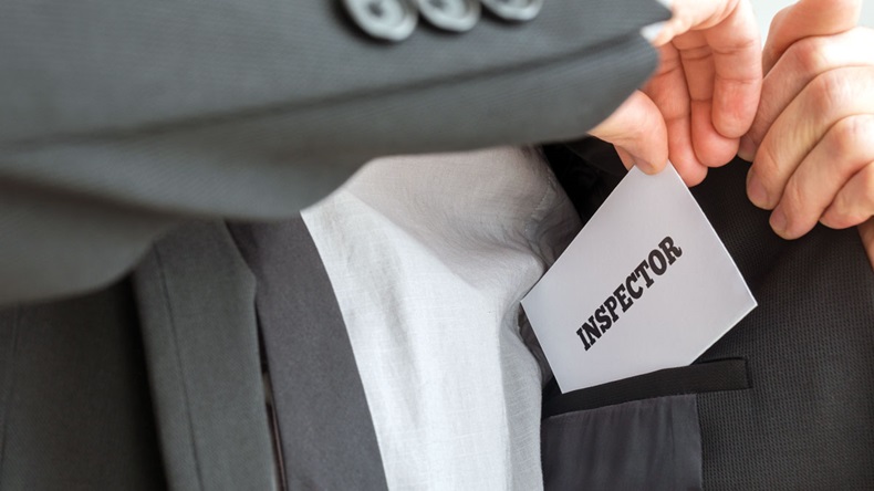 Inspector removing a white card with Inspector sign from the inner pocket of his jacket. Conceptual of health, business or other inspection coming over unannounced.